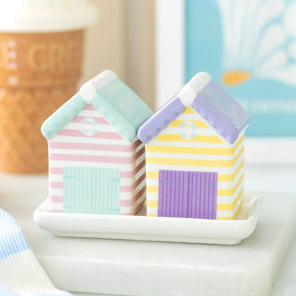 Set of pastel salt and pepper shakers shaped like beach huts on a matching tray with printed coastal details