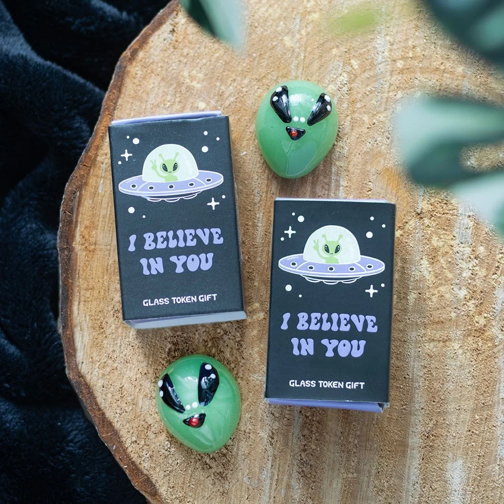 Set of 24 glass alien tokens in green with "I believe in you" matchbox-style packaging in a themed display box