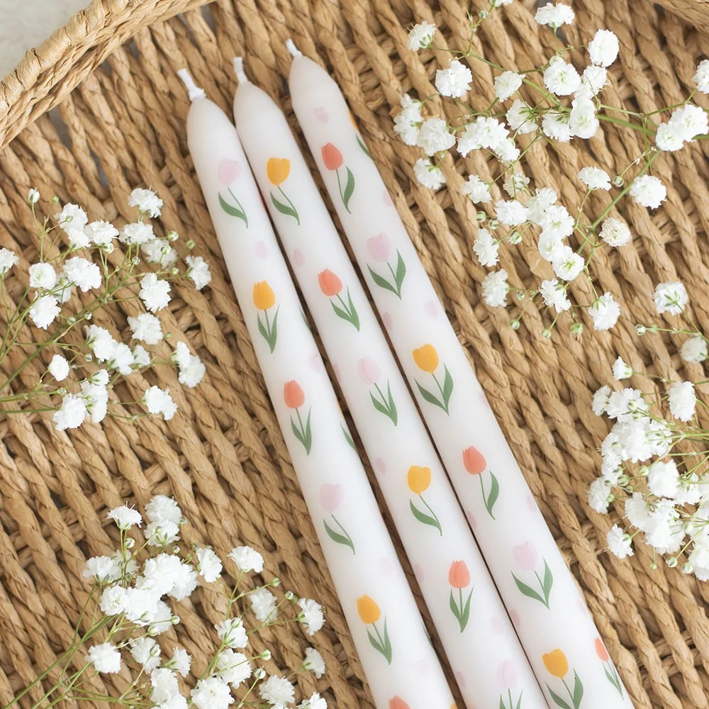 Set of three white tulip print taper candles with delicate floral design on a plain background