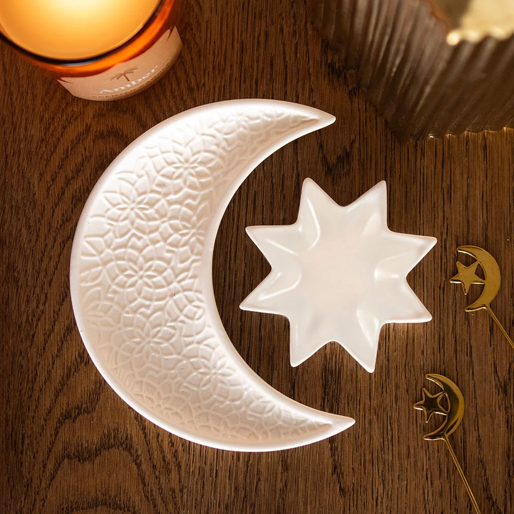 Set of cream ceramic trinket dishes shaped like a crescent moon and star with embossed detailing on a white background