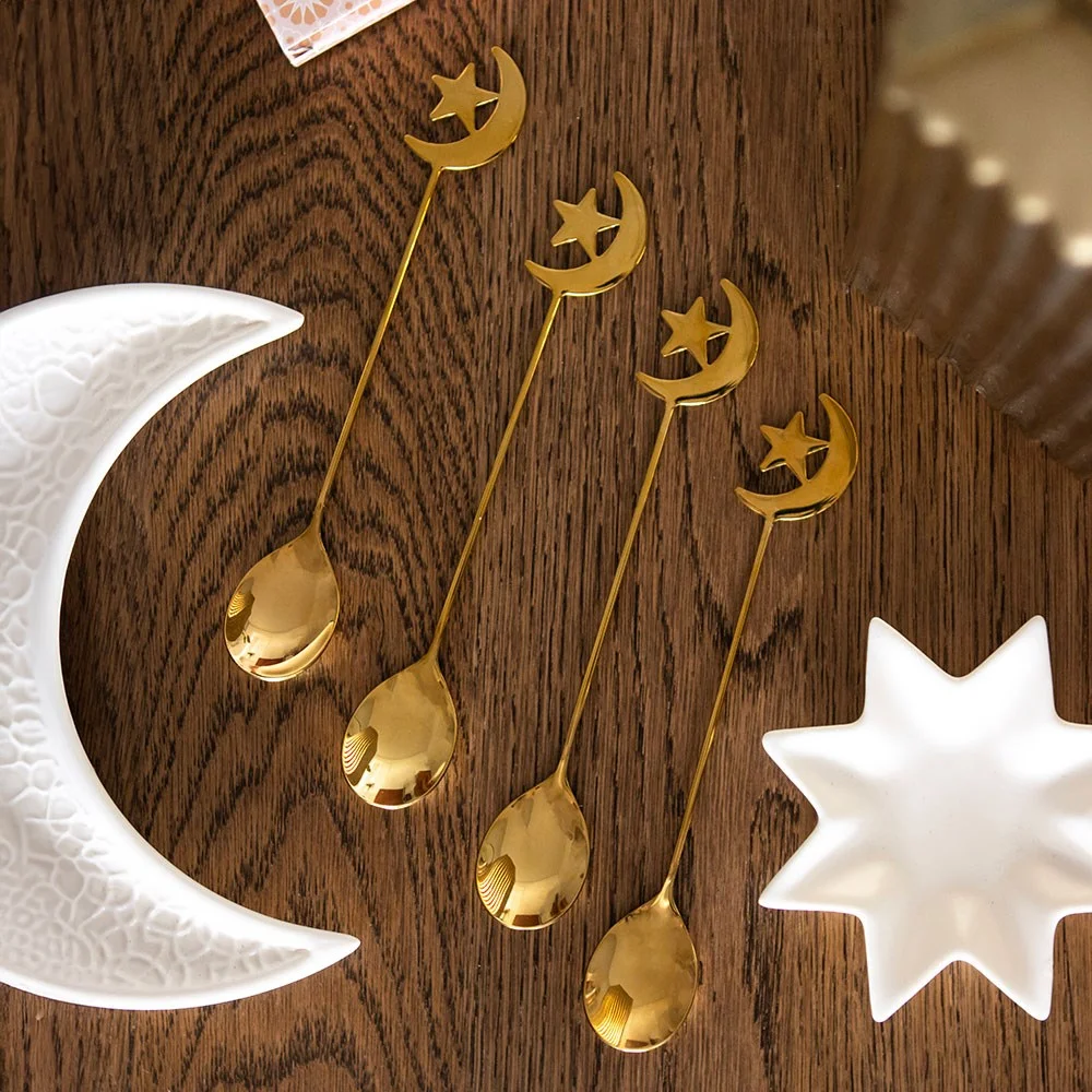 Set of 4 golden teaspoons with star and moon cut-out handles arranged on white background