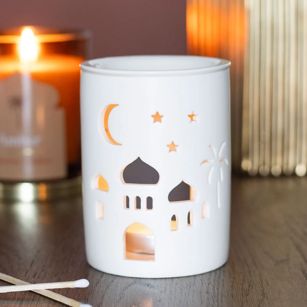 Cylindrical ceramic fragrance burner with intricate cut-out mosque design casting warm light silhouette
