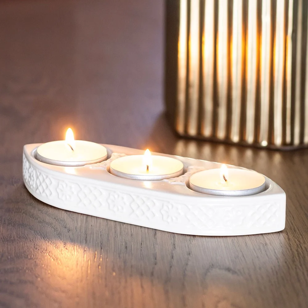 Geometric ceramic tealight holder in neutral tones with space for three lit tealights on a white background