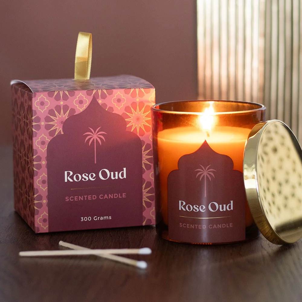 Glass jar rose oud scented candle with sleek design, lit wick, and warm amber glow on neutral background