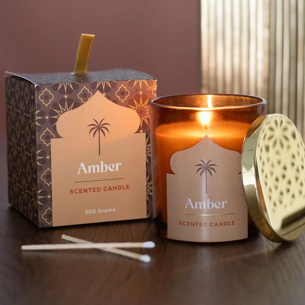 Elegant glass amber scented candle labeled Arabian Nights with warm amber glow on white background