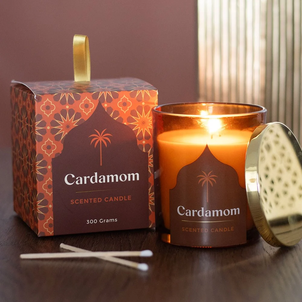 Glass jar with lit Arabian Nights cardamom scented candle emitting warm, spicy glow on plain background