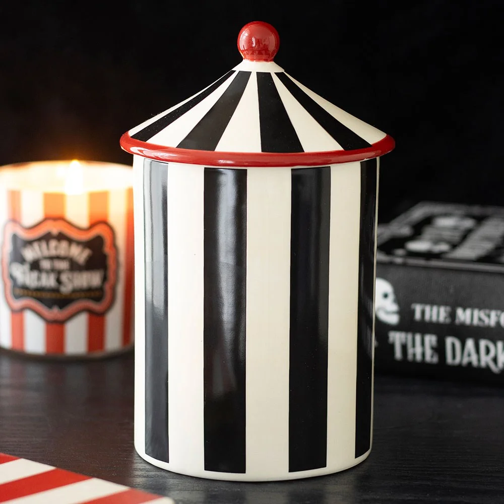 Ceramic storage jar with black stripes and pointed circus tent lid, resting on the counter, for sugar, coffee or snacks.