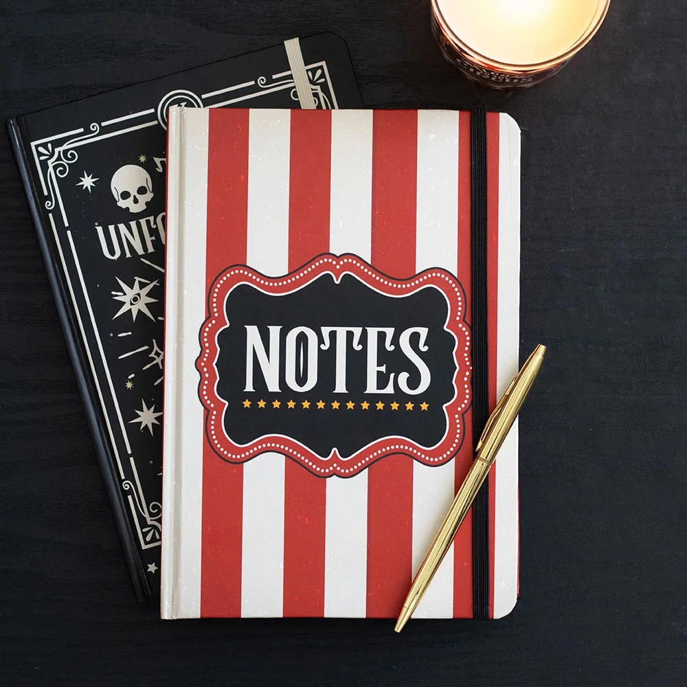 red A5 notebook with bold red stripes on the cover, vintage circus‑themed “NOTES” label, open to lined pages, ribbon marker and elastic closure visible