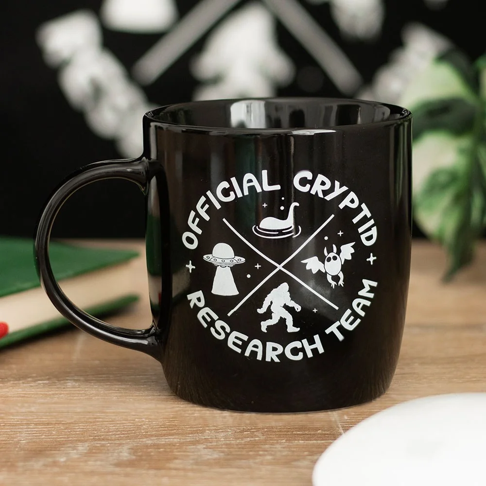 White ceramic cryptid research team mug with black mysterious creature design and official text, 350ml capacity.