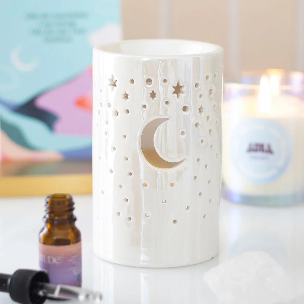 Iridescent white ceramic moon pillar oil burner with cut-out stars and crescent moon, lit with tealight inside