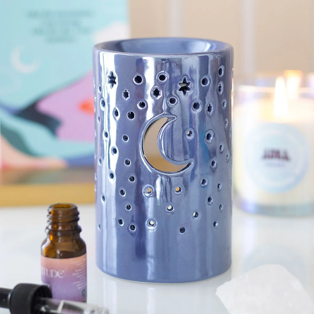 Iridescent purple oil burner with moon and star cut-outs glowing, ceramic pillar shape for wax or fragrance oils