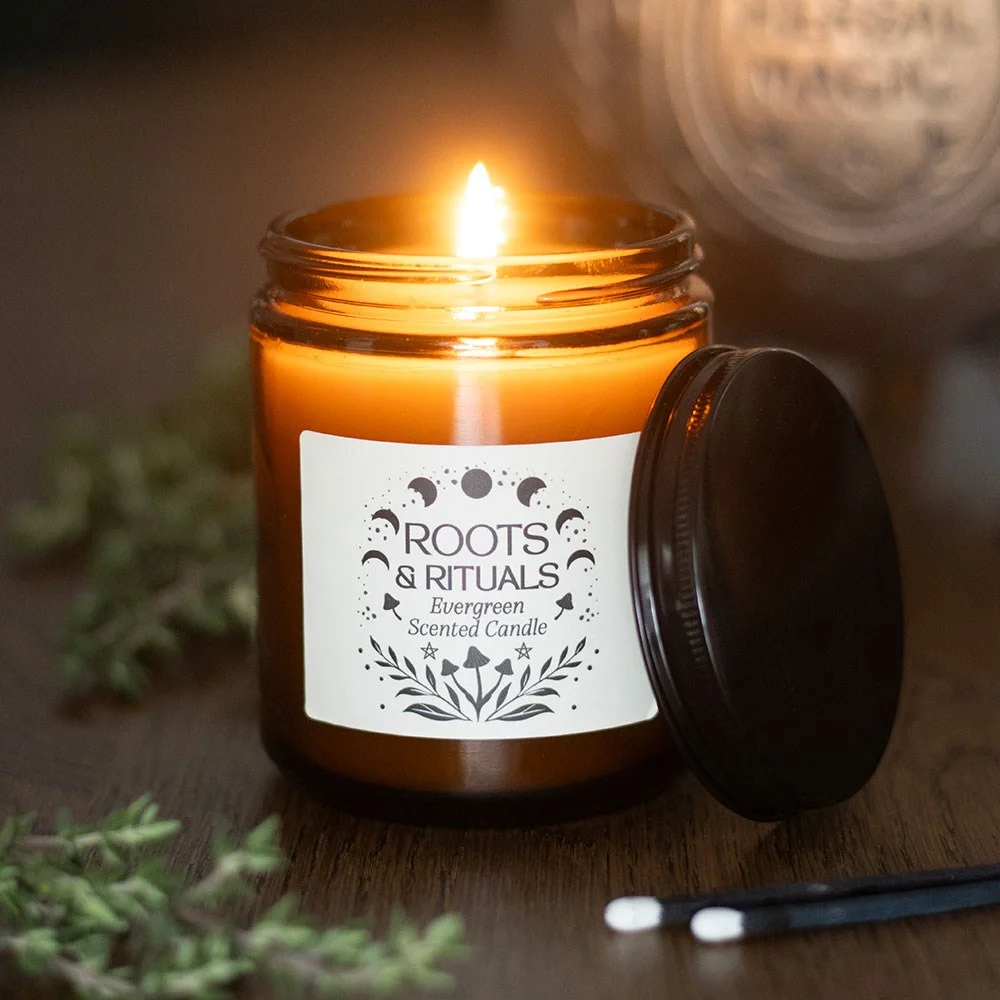 Evergreen scented candle in amber glass jar with Roots & Rituals label, bulb light visible through melted wax.
