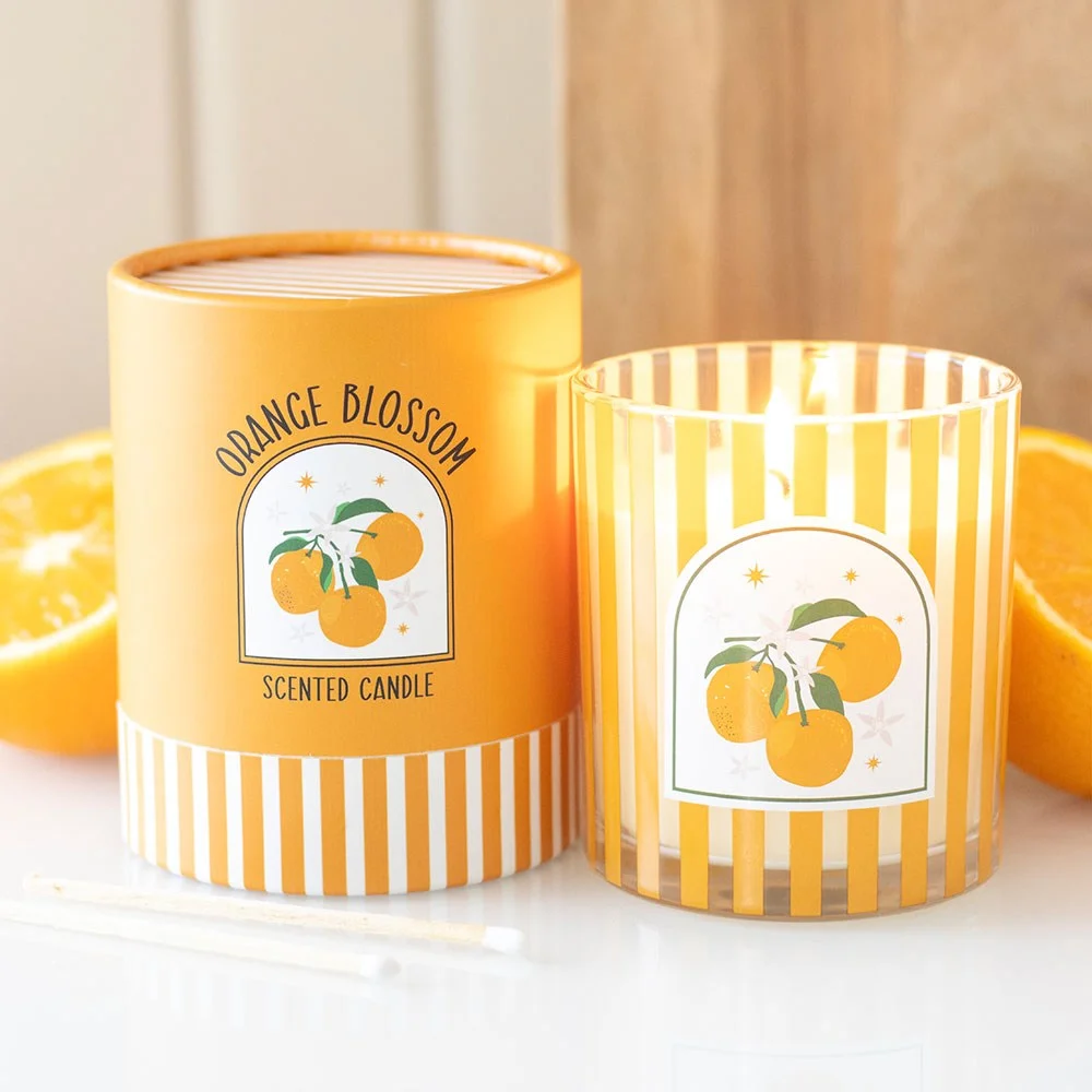 Orange blossom scented candle in a bold striped glass jar, bright orange flame illuminating a sunny interior.