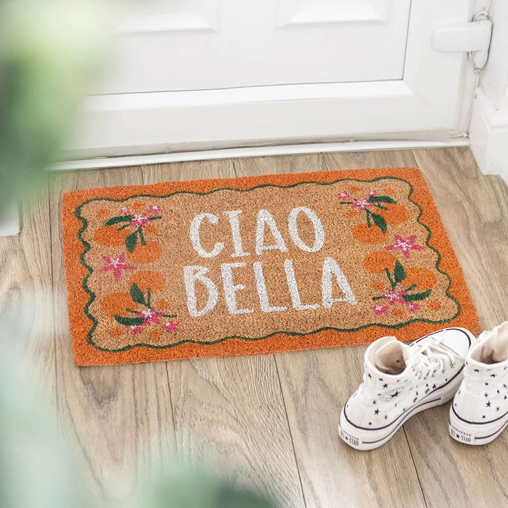 Orange coir doormat with bright orange borders, citrus fruit design and playful Ciao Bella phrase, displayed on a porch.