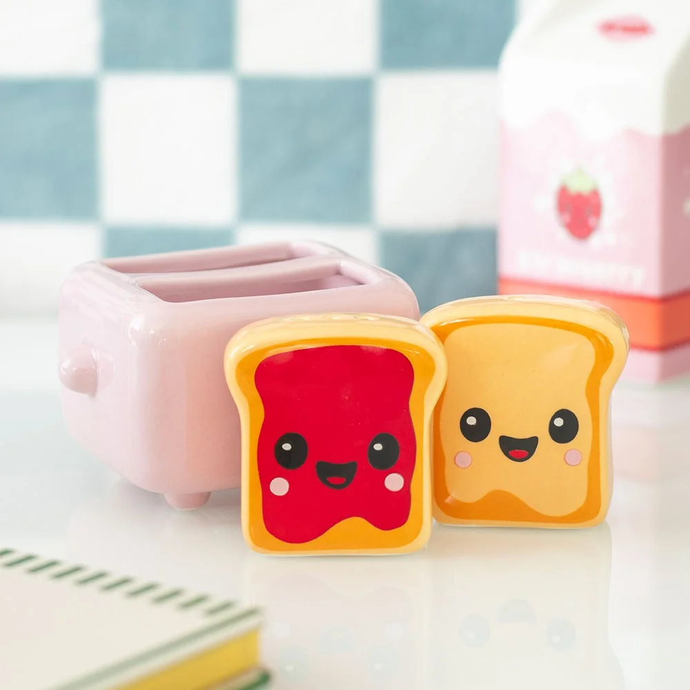 Kawaii salt and pepper shakers with peanut butter and jelly toast characters, ceramic, in pink toaster-shaped holder. Cute decor.
