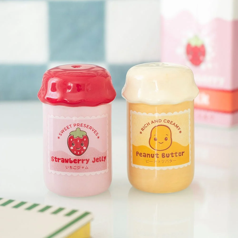 Two ceramic salt and pepper shakers shaped like peanut butter and strawberry jelly jars with smiling faces and bright colours.
