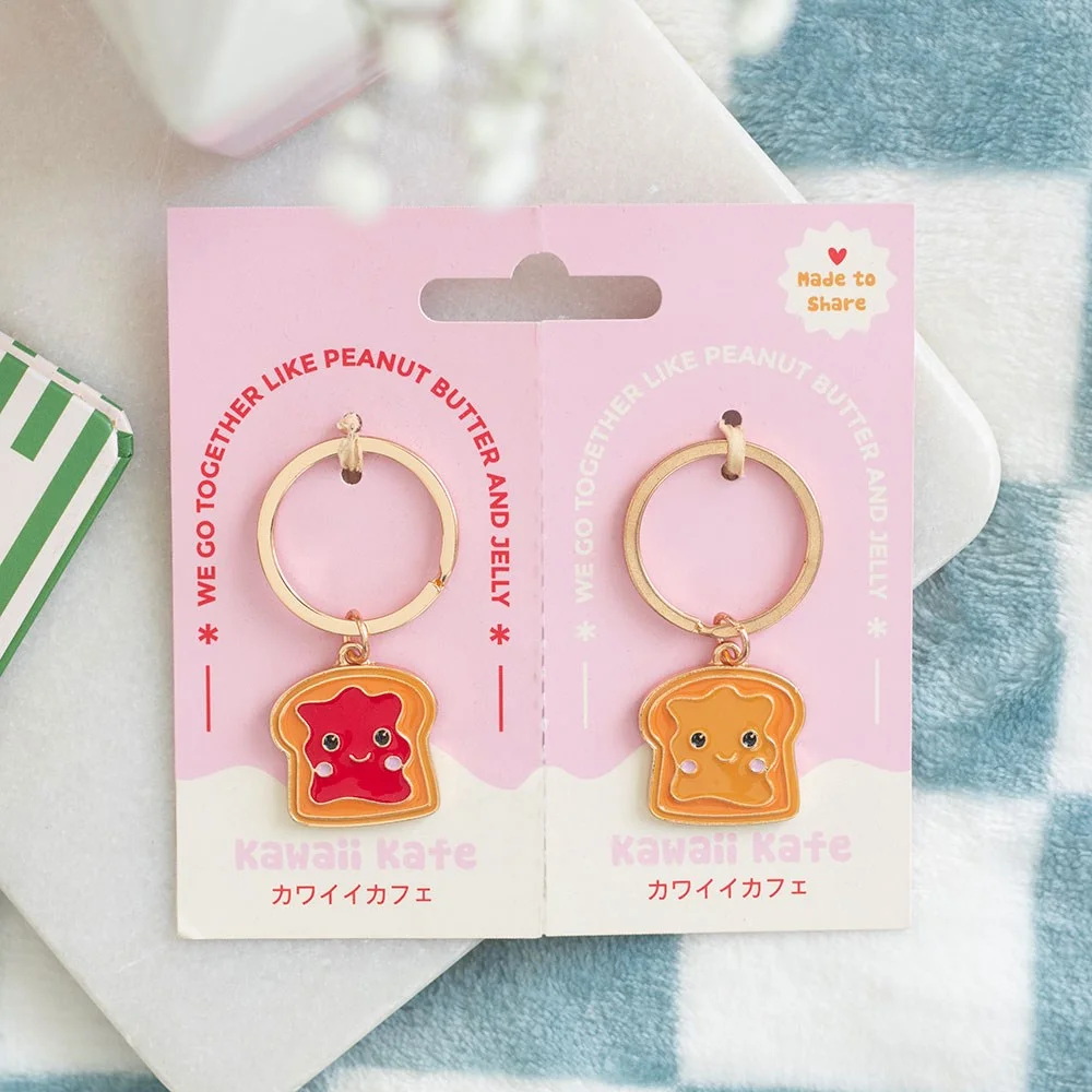 Two peanut butter jelly keyrings displaying smiling toast charms in glossy enamel.