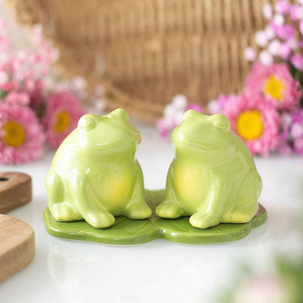 Set of two ceramic salt and pepper shakers shaped like playful green frogs on a white background
