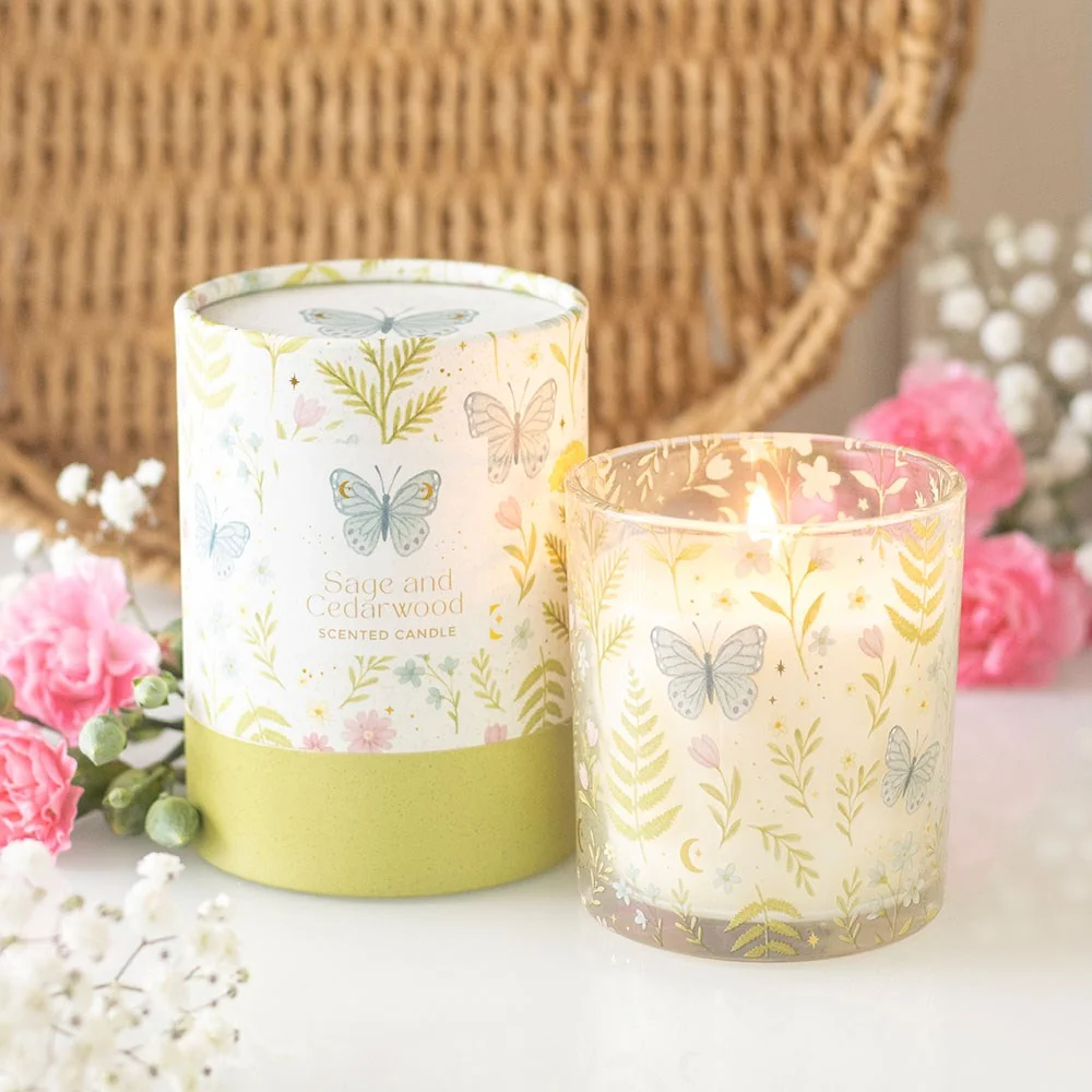Sage cedarwood candle in glass holder surrounded by pastel florals and fluttering butterflies.