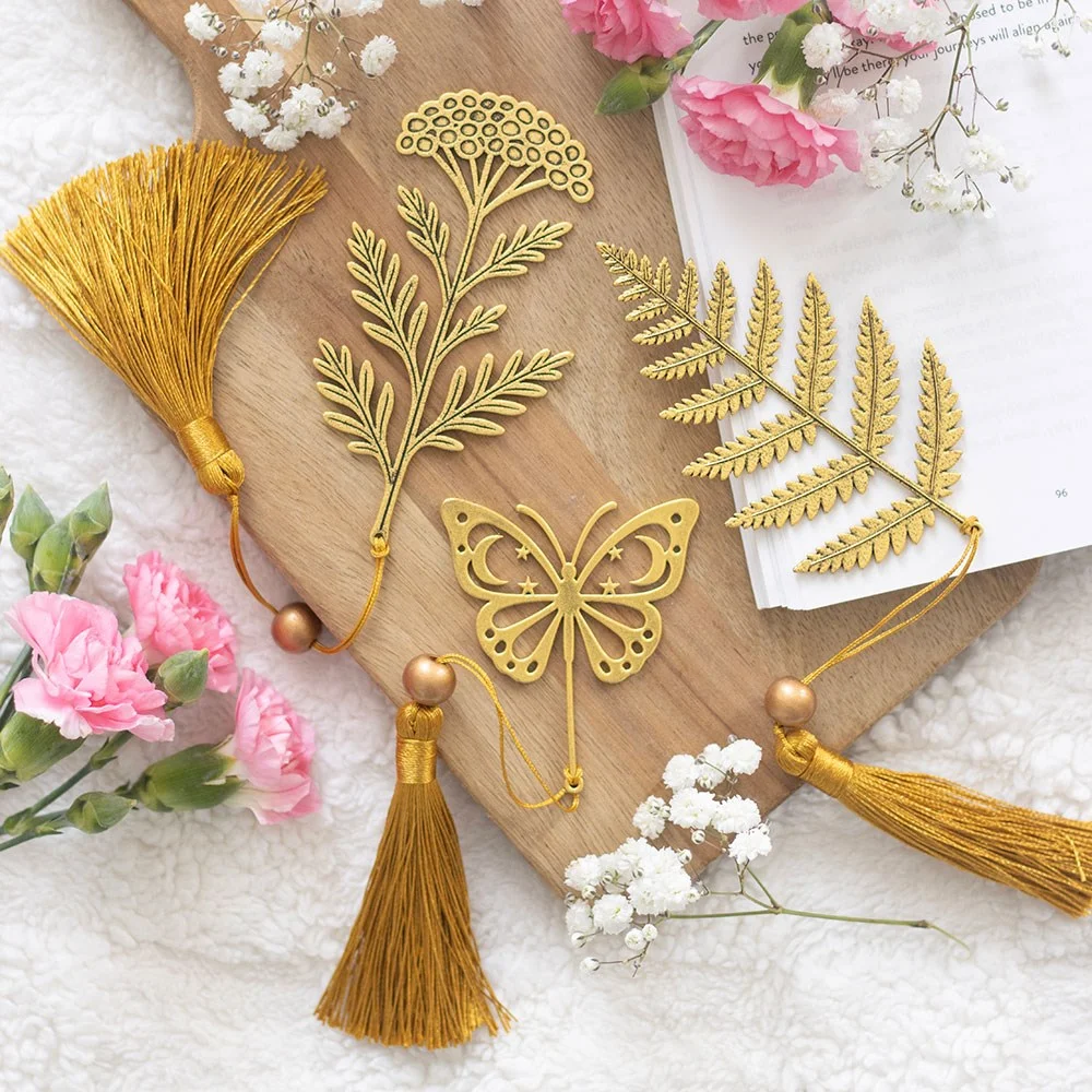 Set of 24 metal leaf bookmarks featuring fern, butterfly, and wildflower designs with matching tassels on white background