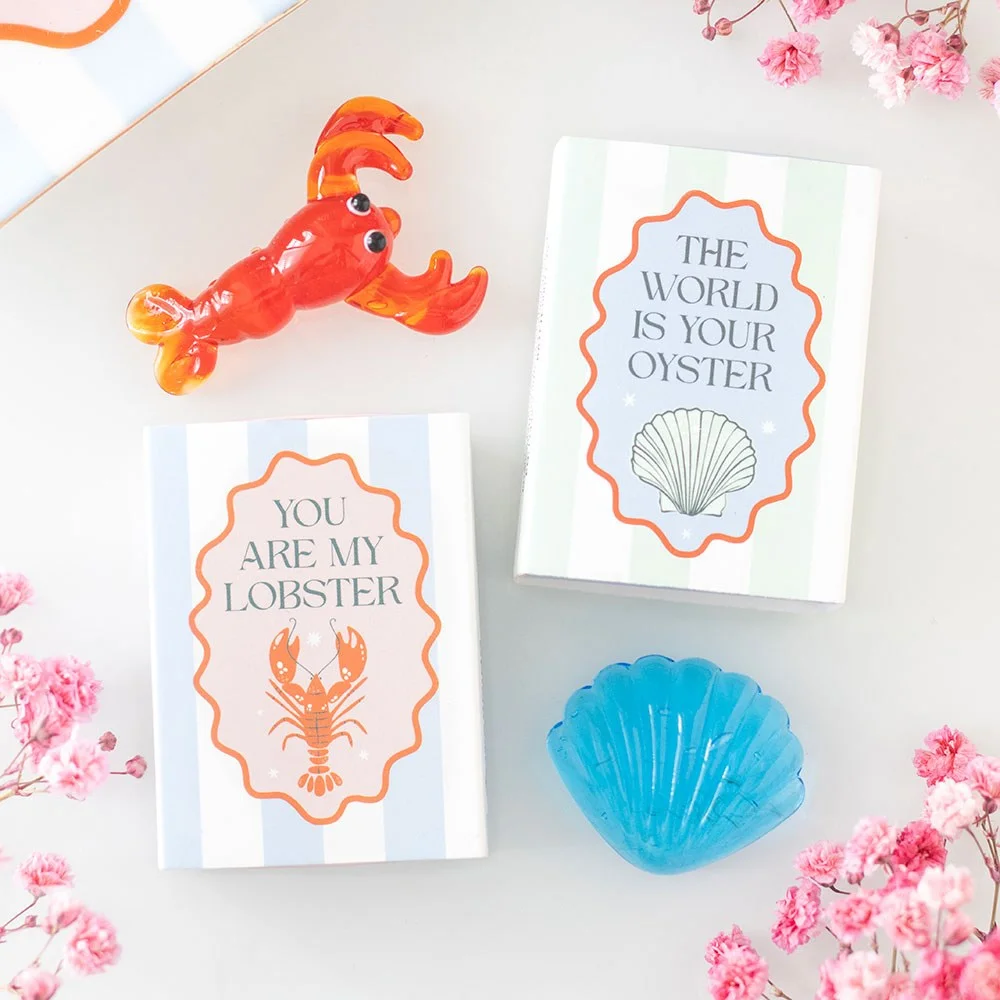 Set of 24 nautical glass token gifts in pastel shades with coastal designs and phrases, displayed in a neat box set