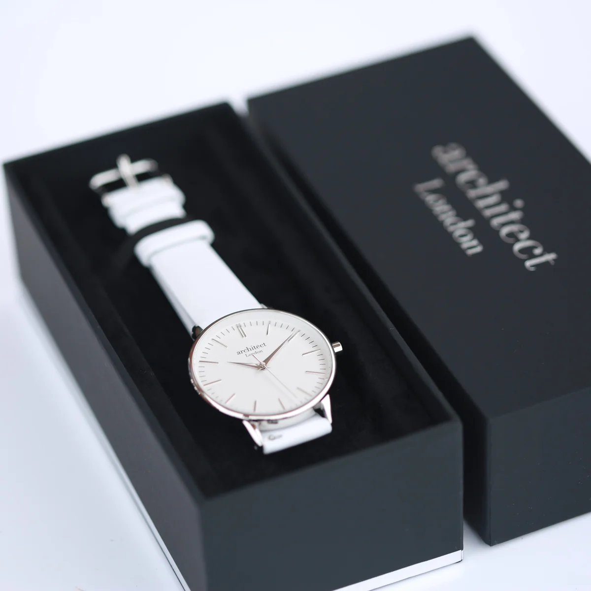 Ladies silver bezel watch with white leather strap and minimalist white dial, displayed on a white background