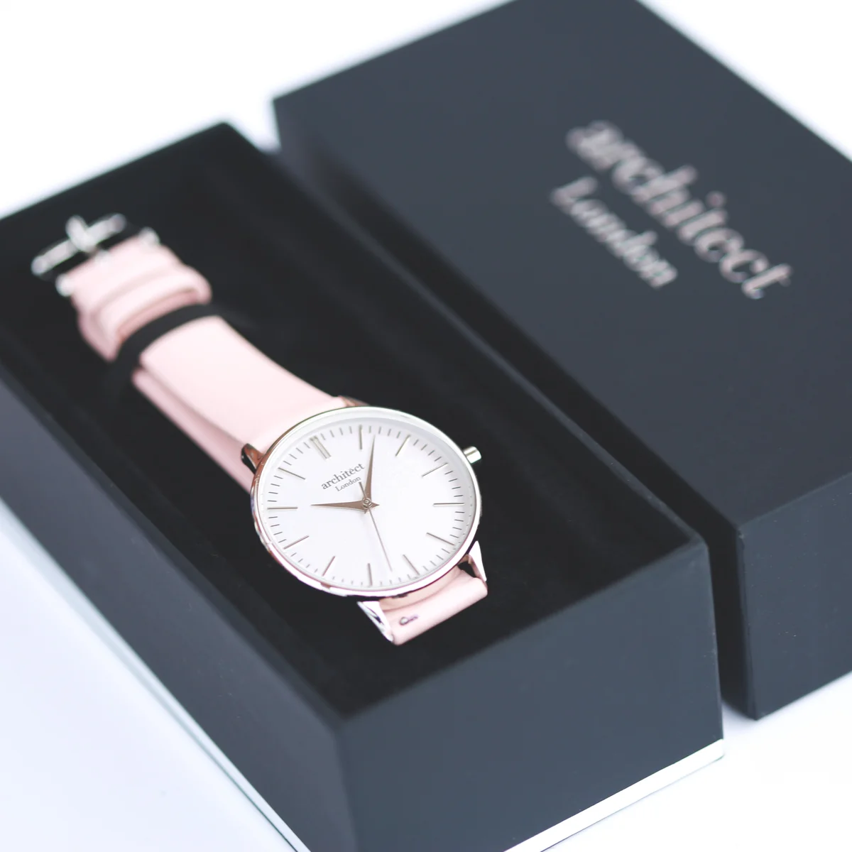 Ladies silver bezel watch with light pink leather strap and minimalist white dial, modern font engraving visible on back