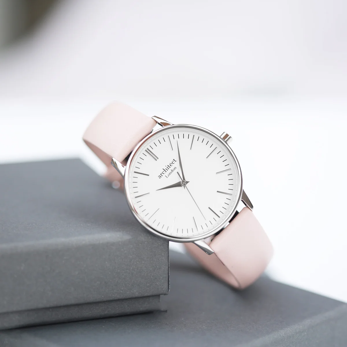 Engraved ladies watch with silver bezel, light pink leather strap, modern font engraving on back, displayed flat on white background