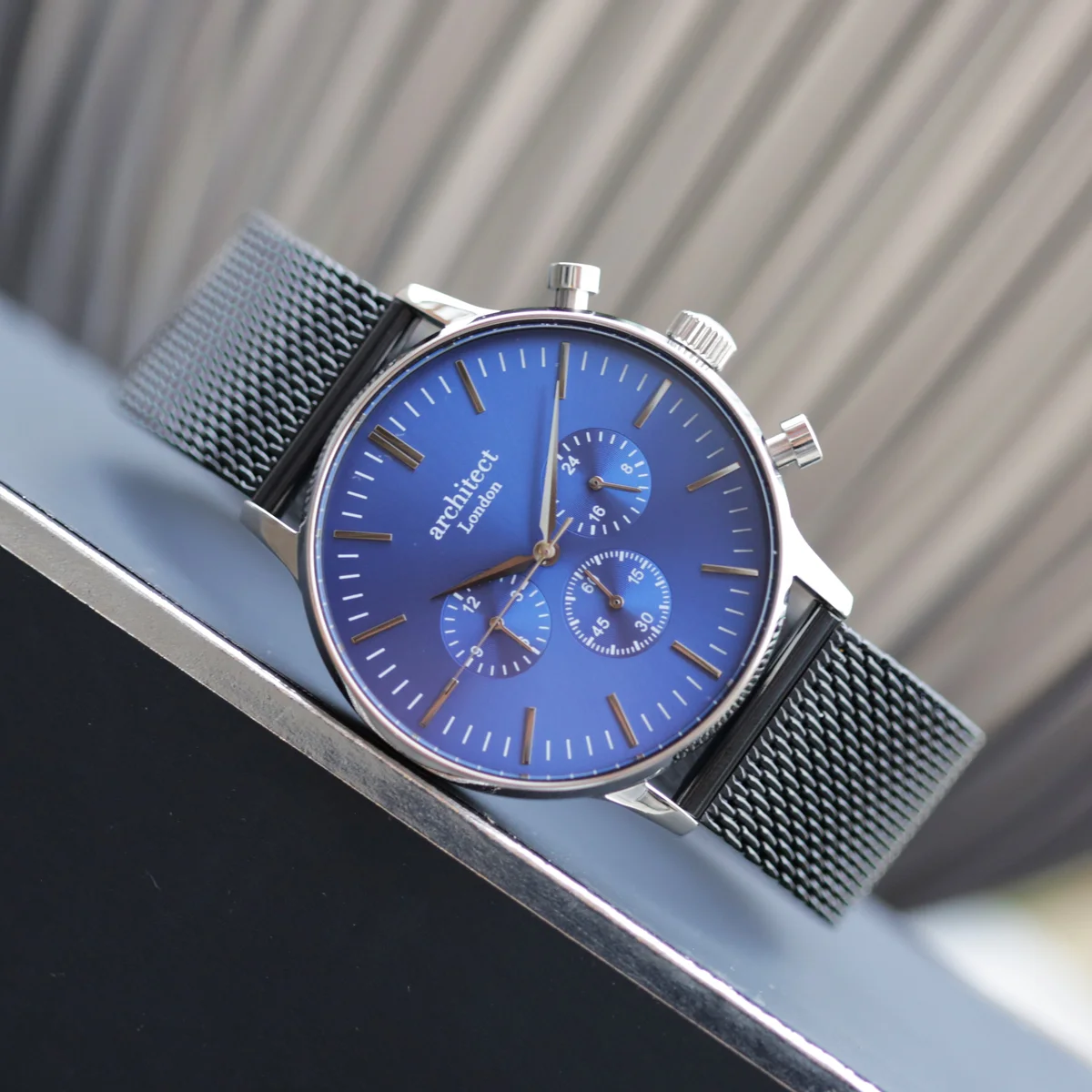Deep-space blue engraved men's watch with black Milanese mesh strap and three chronograph subdials on white background