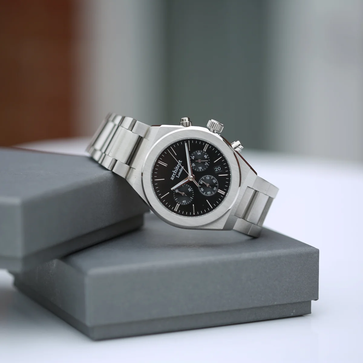 Black dial men's watch with stainless steel case, silver bracelet, chronograph subdials, and modern font engraving area on back