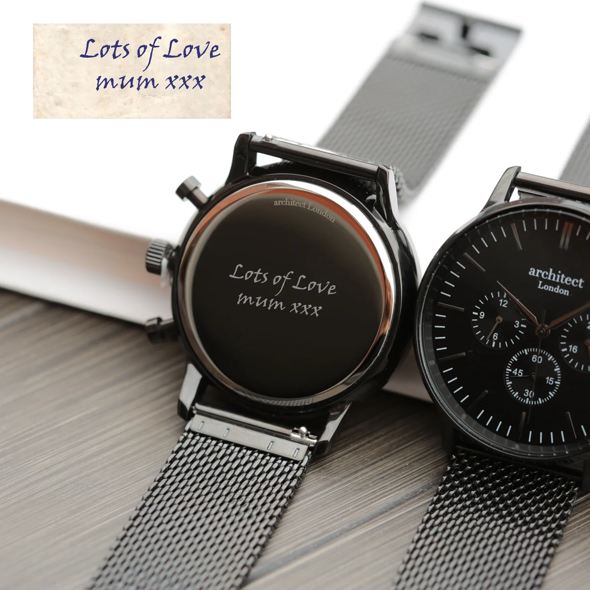 Black face engraved men's watch with three chronograph subdials and black Milanese mesh strap on white background