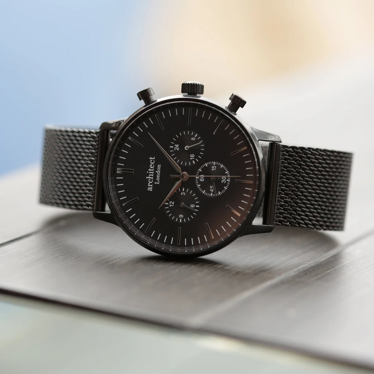 Men's personalised watch with black dial, three chronograph subdials, and black Milanese mesh strap on white background