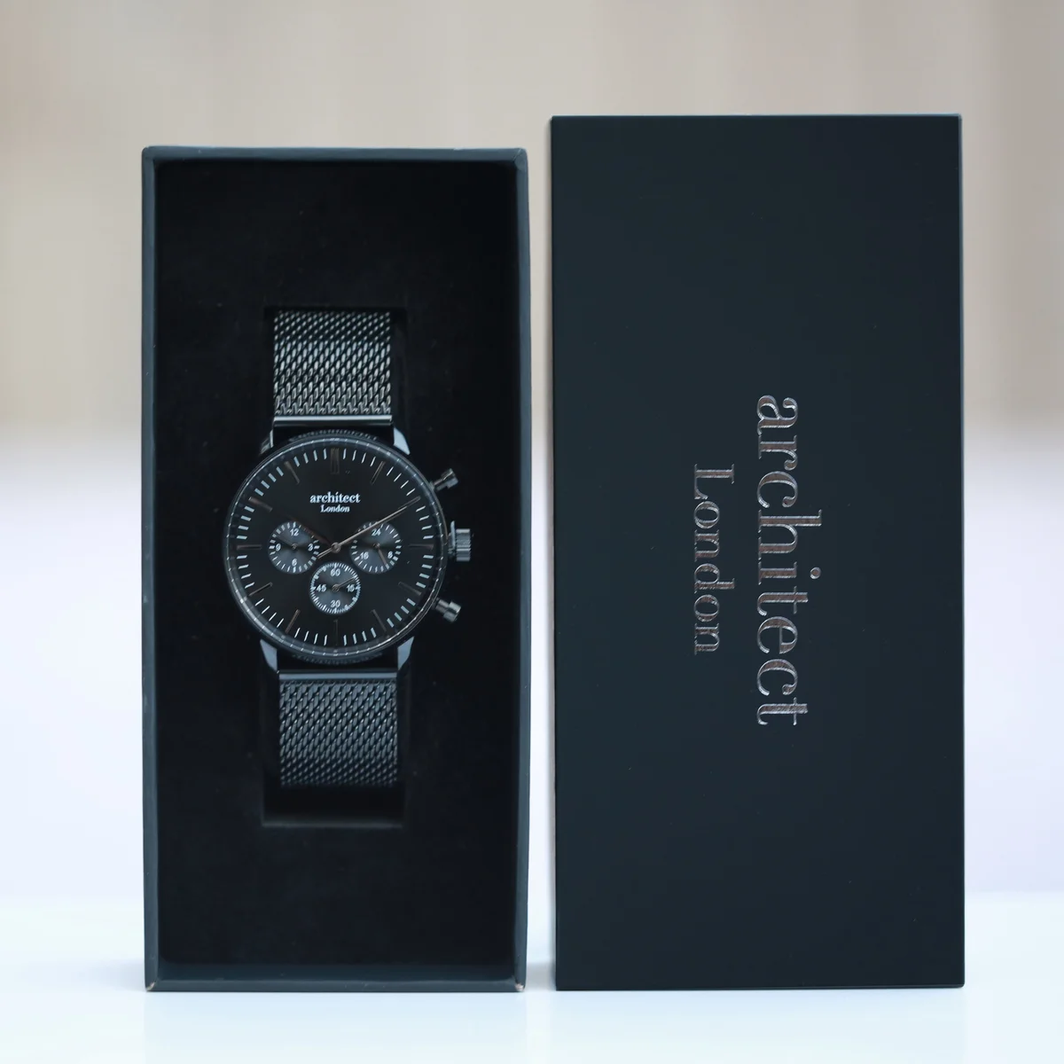 Black stainless steel watch mens with black Milanese mesh strap and three chronograph subdials on white background
