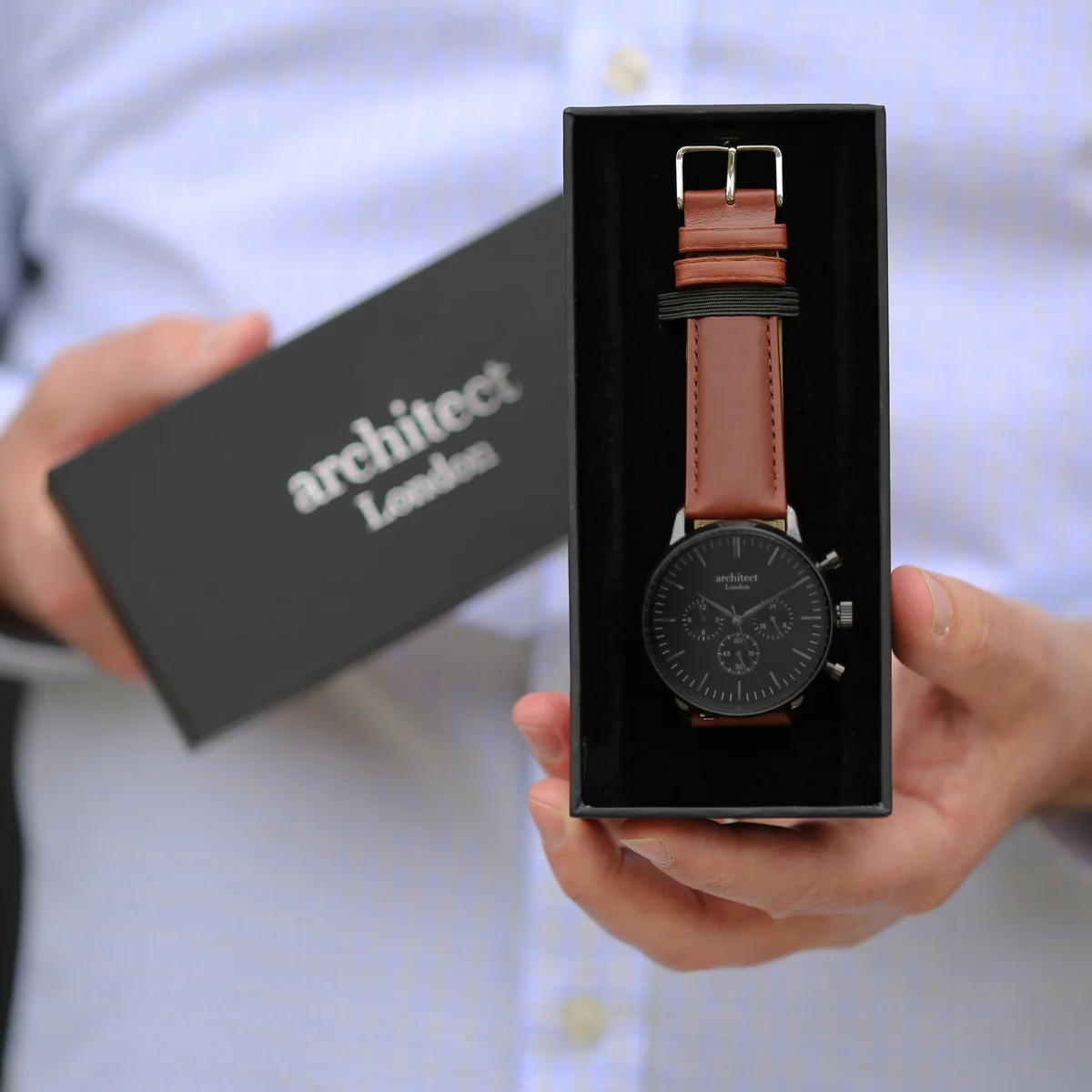 Black quartz movement watch with walnut brown leather strap and three chronograph subdials on white background