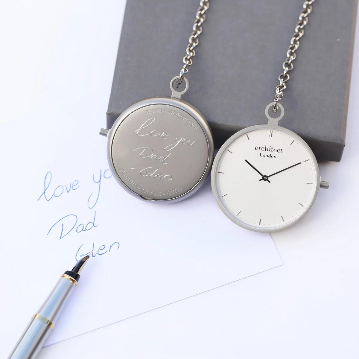 Modern silver pocket watch with brushed stainless steel case, sapphire glass, and clear dial showing Swiss movement mechanism