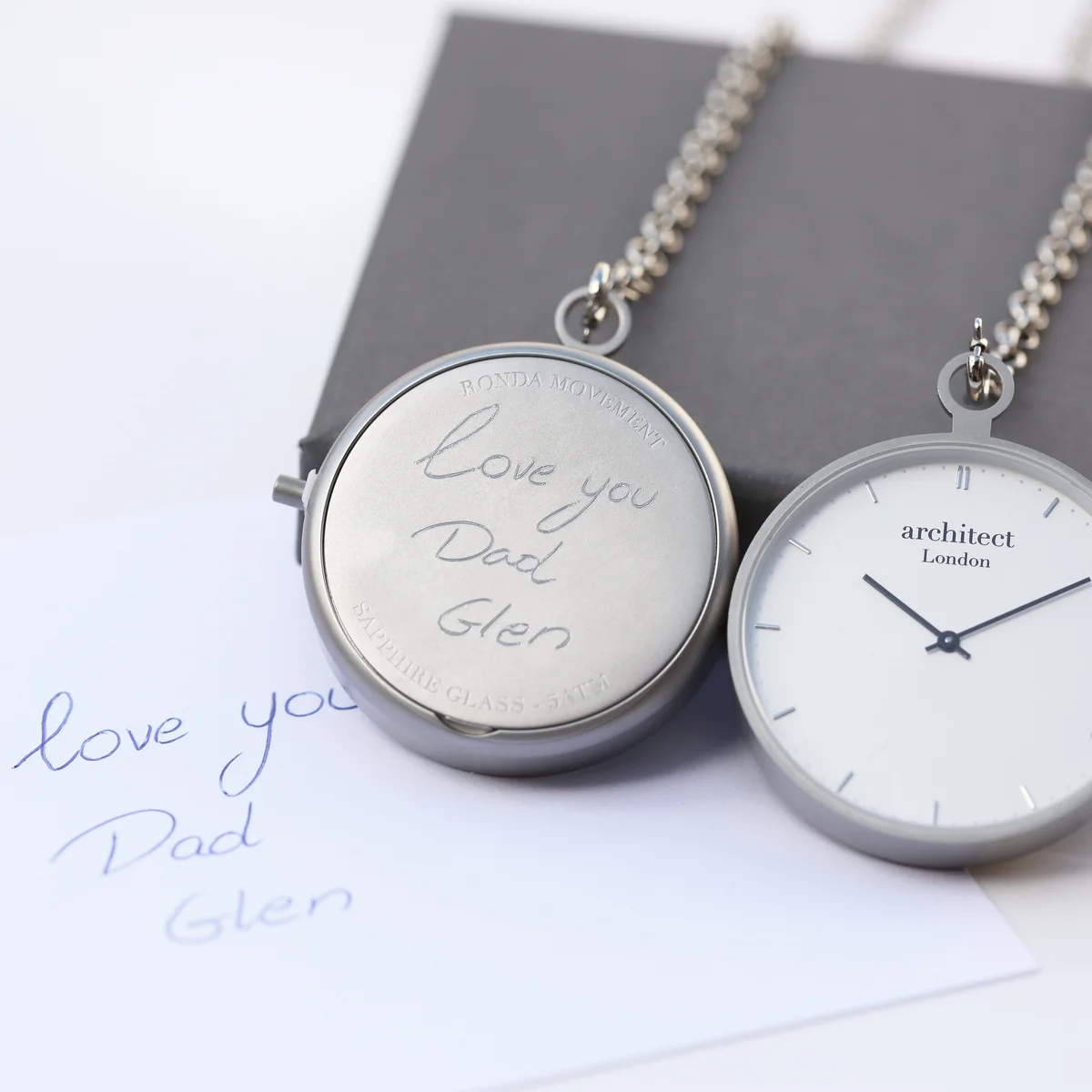 Modern pocket watch with brushed silver case and clear sapphire glass, showing detailed Swiss movement inside