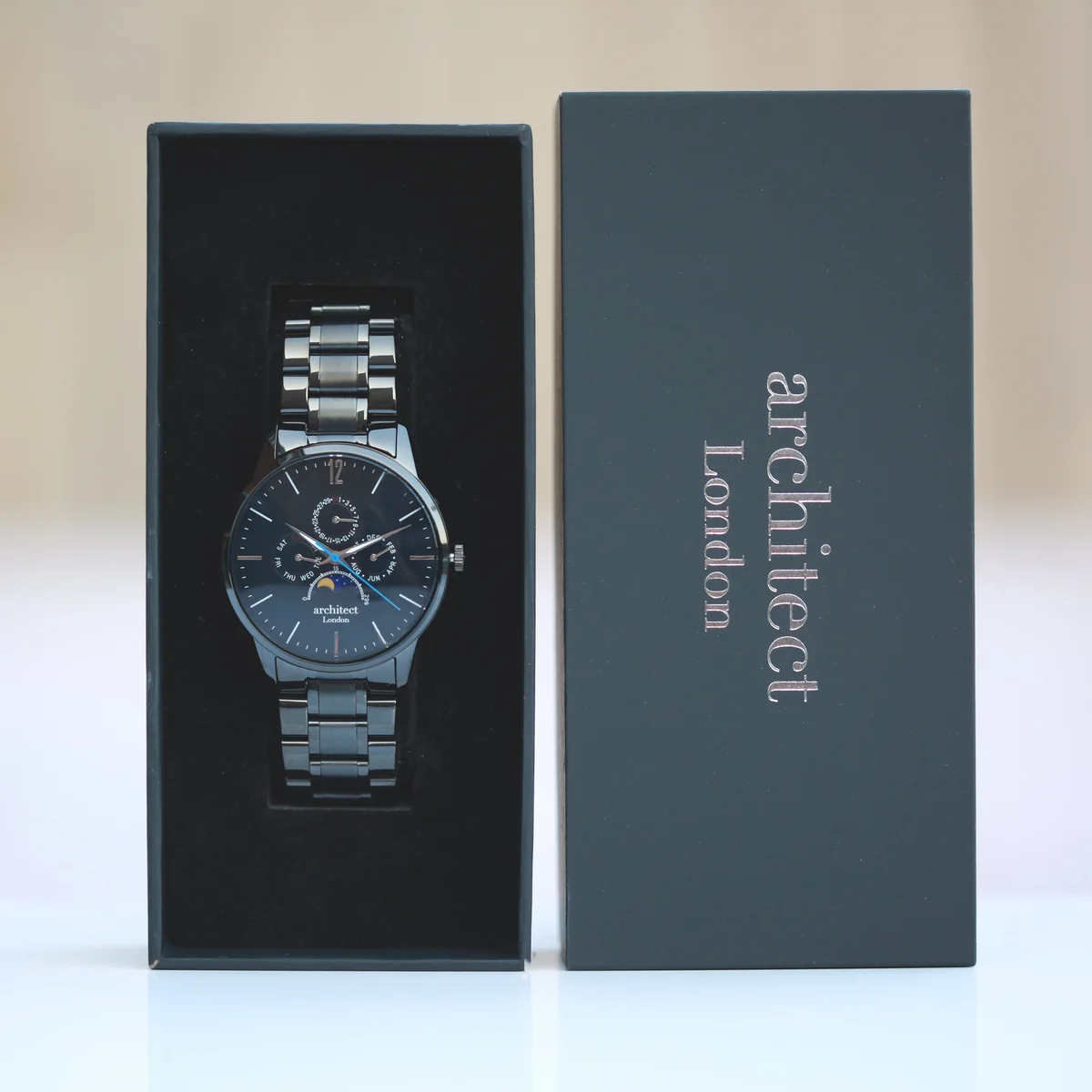 Black chronograph watch with moonphase dial, polished stainless steel case, and black stainless steel strap on white background