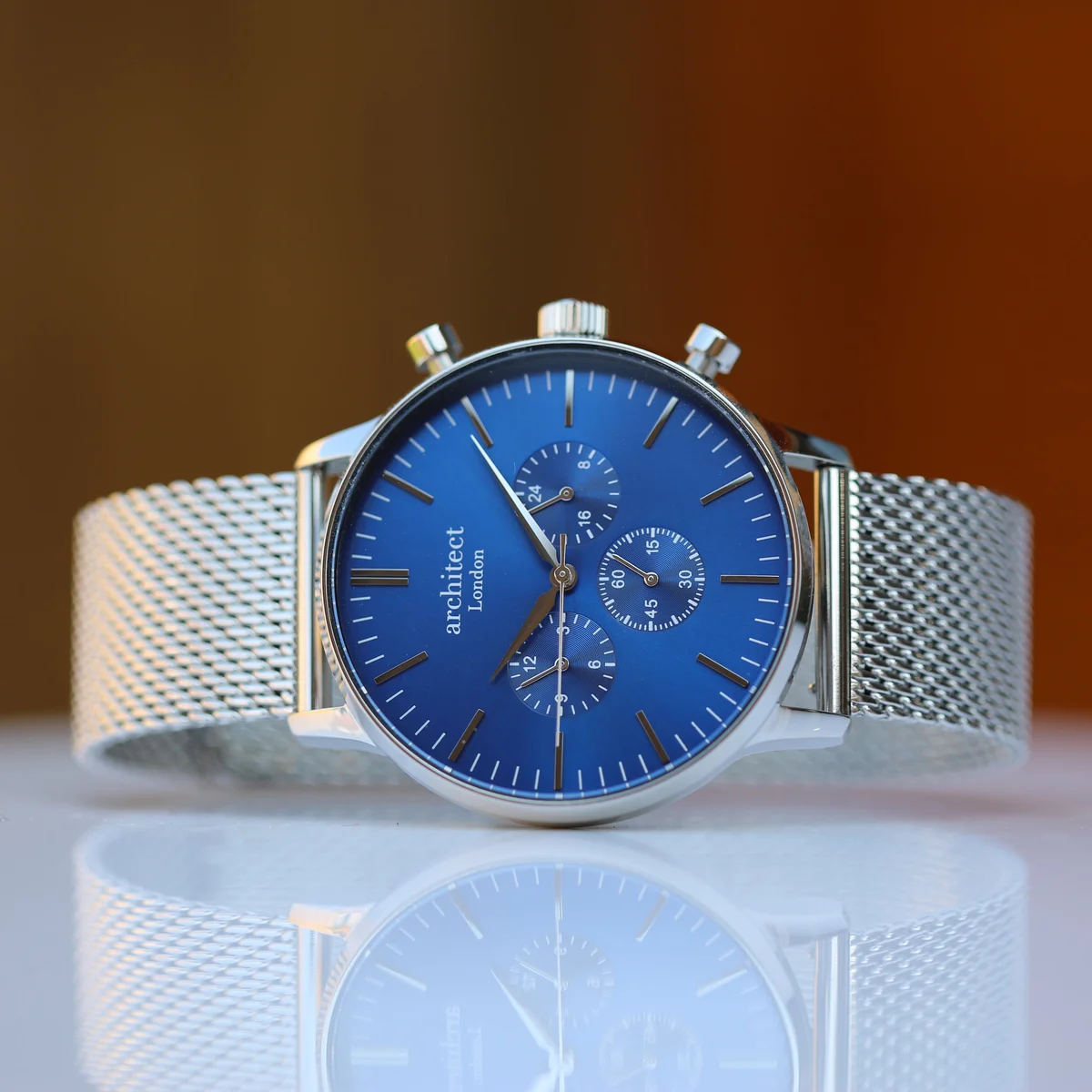 Engraved men's watch with deep-space blue dial, silver Milanese mesh strap, and three chronograph subdials on wrist