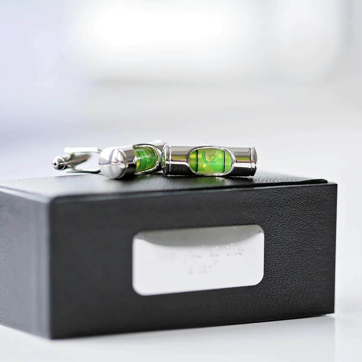 Pair of spirit level cufflinks with liquid detail displayed next to an engraved cufflink box with personalised message