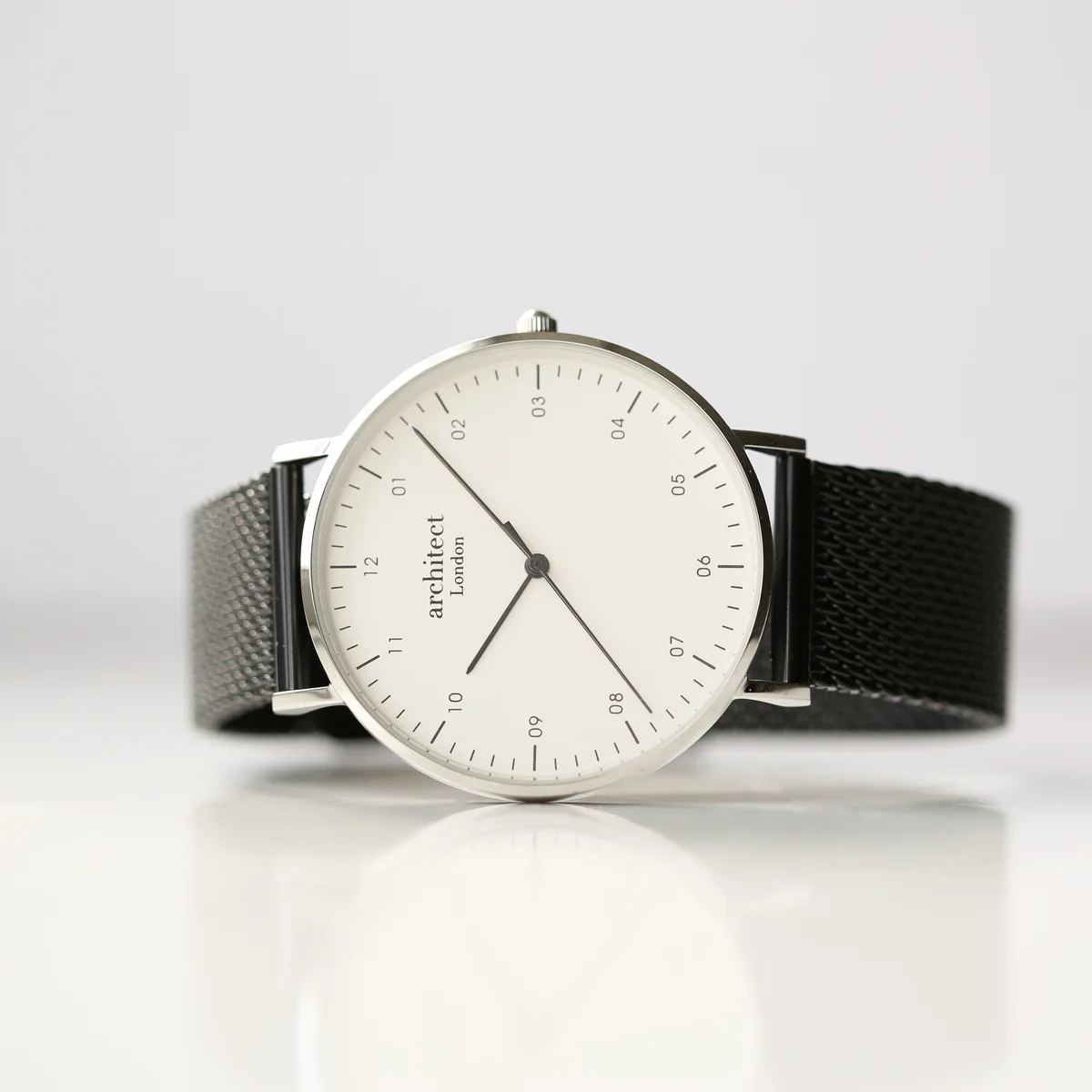 Men's minimalist watch with polished stainless steel case, black mesh strap, and modern font engraving option