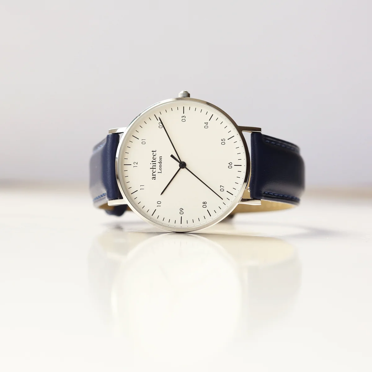 Men’s minimalist leather strap watch with polished stainless steel case and Admiral blue quick-release band on white background