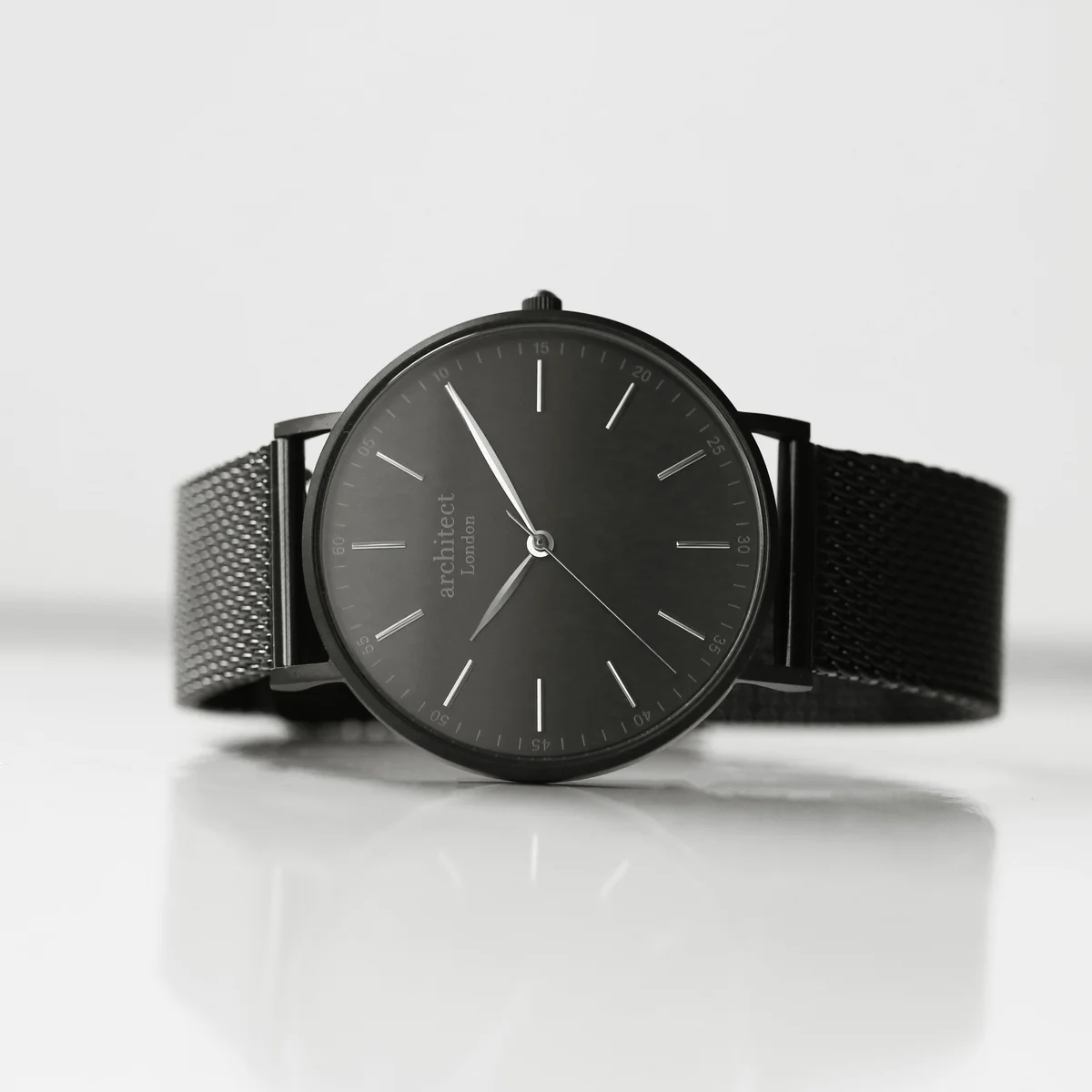 Men's minimalist black mesh strap watch with brushed stainless steel case and clean dial on white background