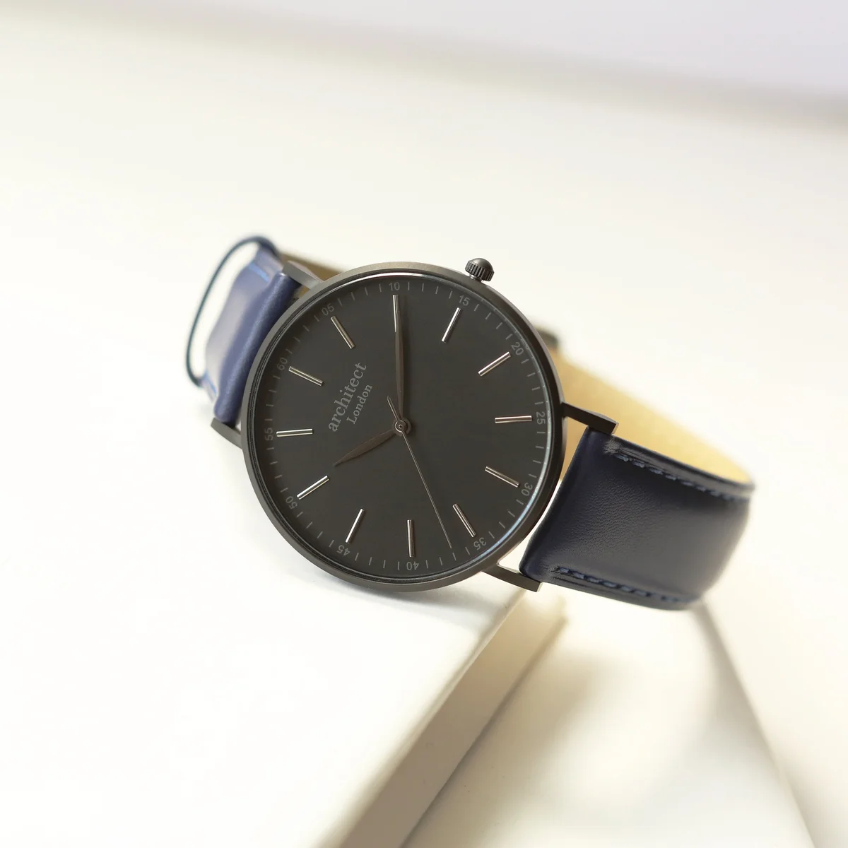 Men's minimalist watch with admiral blue leather strap and stainless steel case on white background