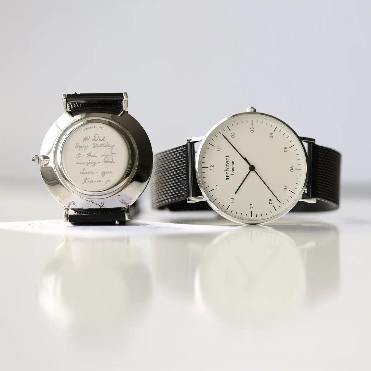 Men's minimalist watch with polished stainless steel case, black mesh strap, and custom handwriting engraving on back