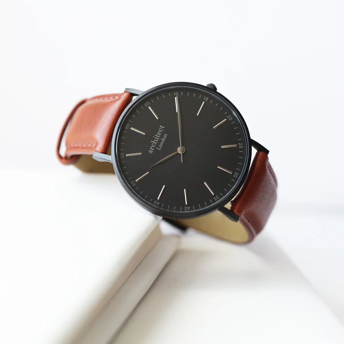 Men's minimalist watch with walnut leather strap, stainless steel case, and clean dial on white background