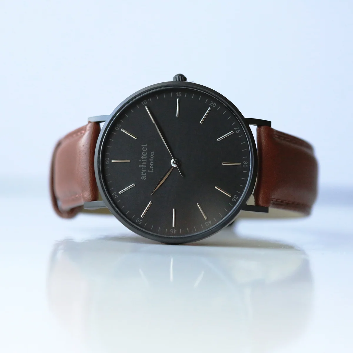 Engraved wristwatch with minimalist dial, walnut leather strap, and brushed stainless steel case on white background