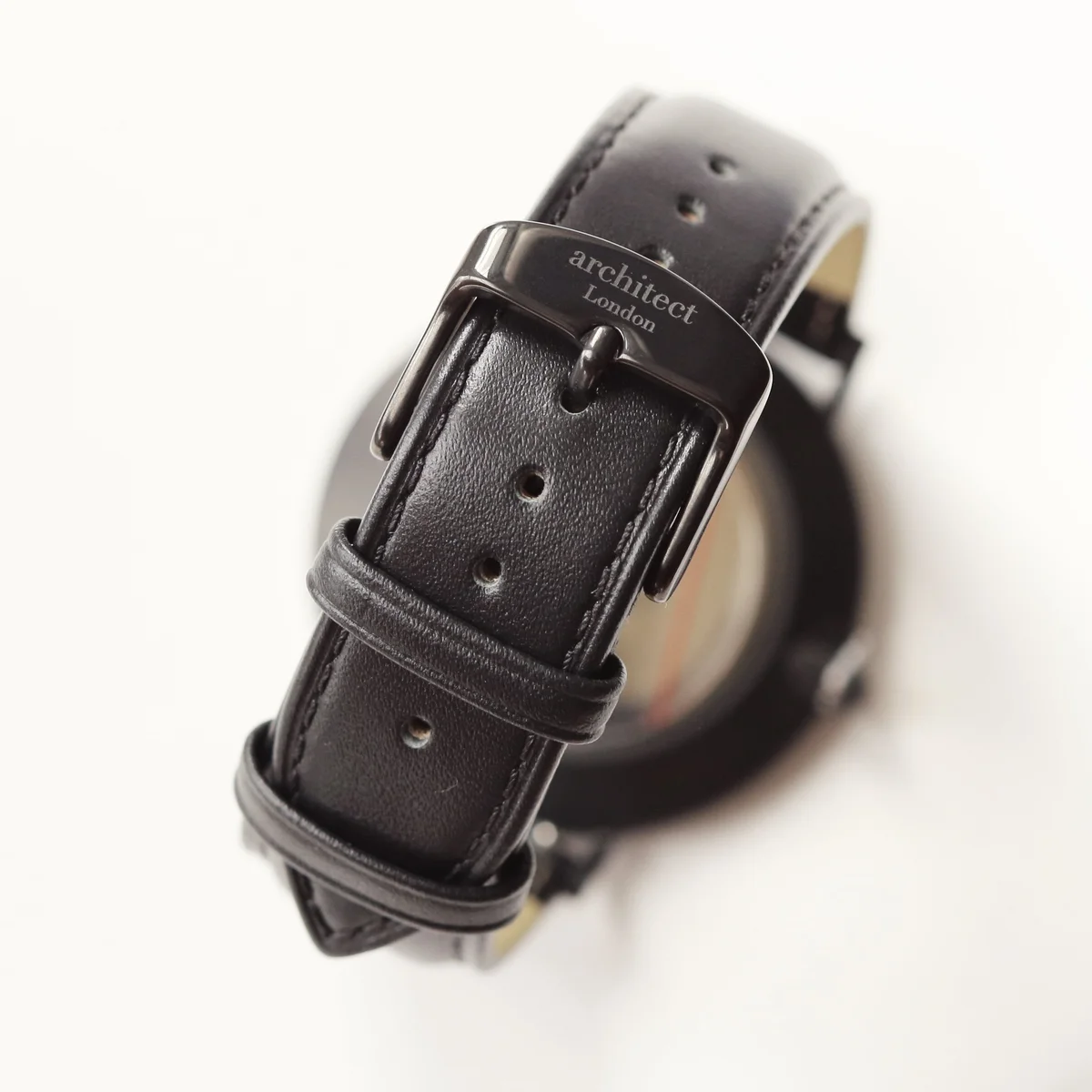 Minimalist stainless steel watch with black leather strap and modern font engraving on case back, displayed in luxury box