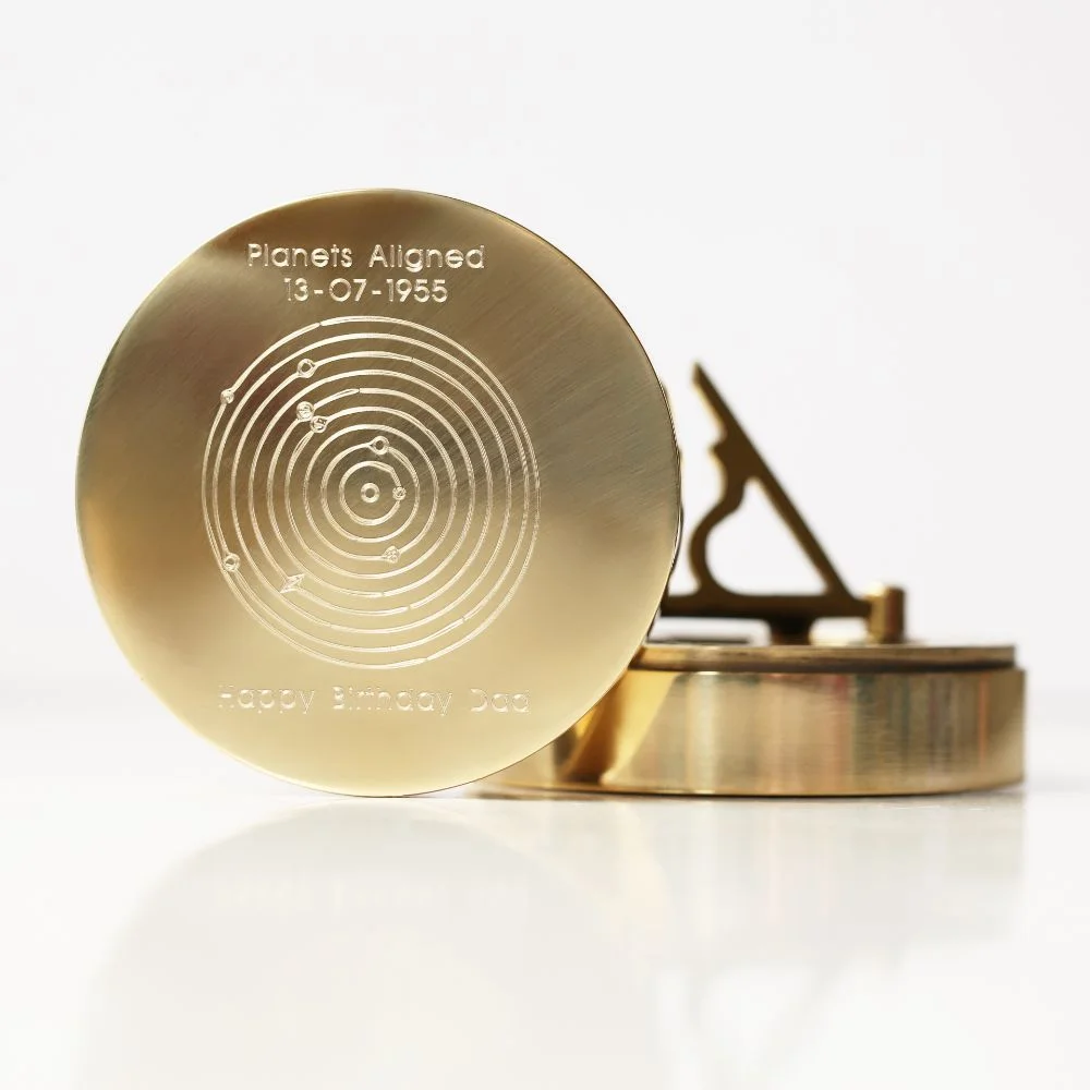 Brass sundial compass with engraved planets alignment and date, shown with protective pouch and gift box on white background