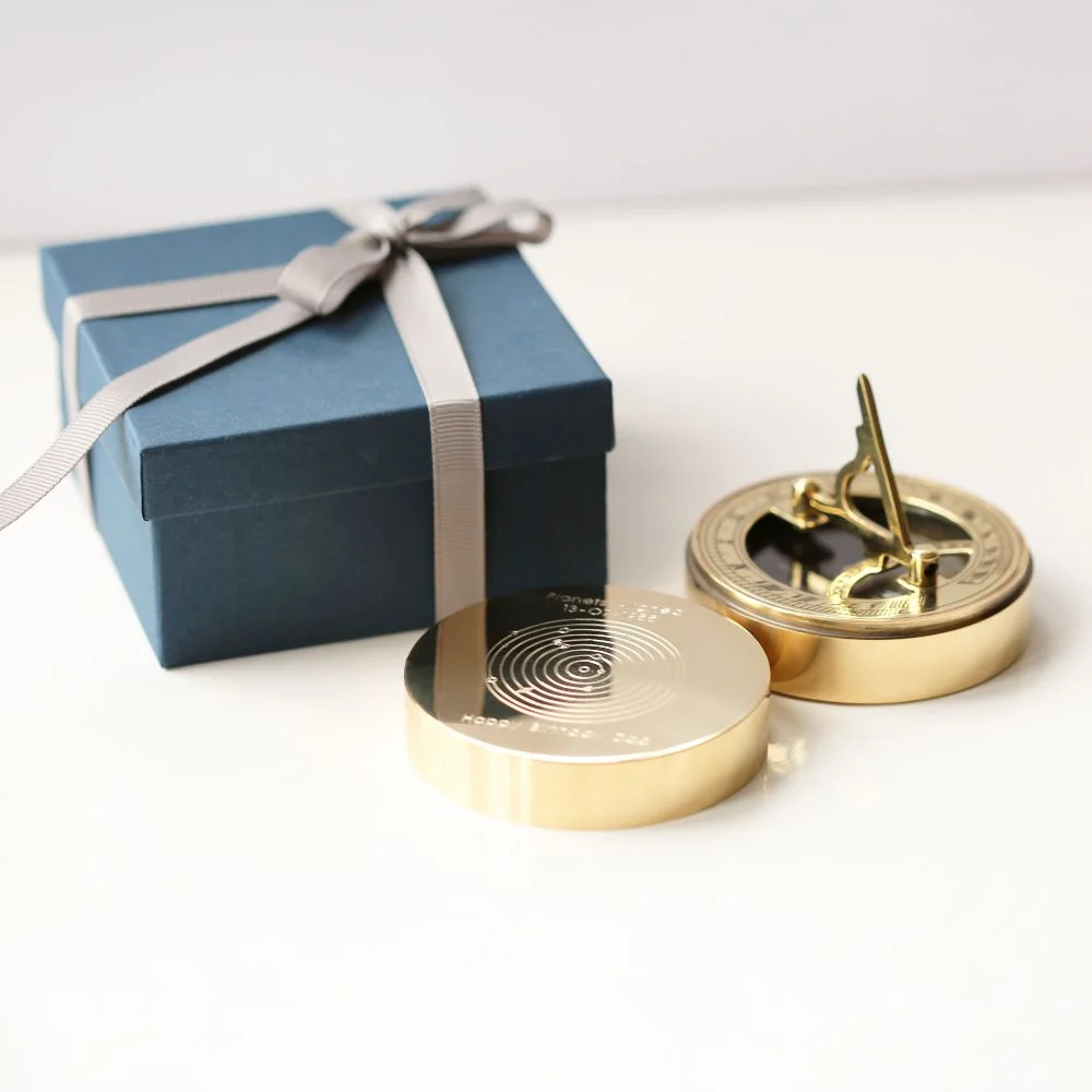 Brass planets aligned compass showing engraved date, with protective pouch and gift box on white background