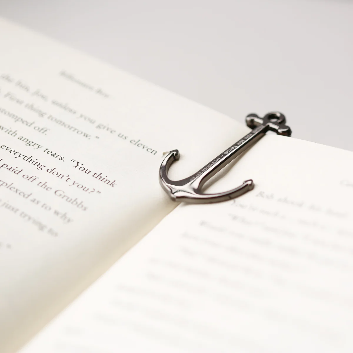 Personalised book anchor in silver and black polished metal holding open a book, displayed with gift box on white background